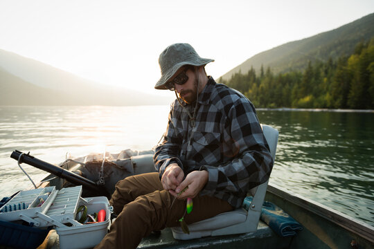 Man fishing on lake, preparing tackle box in boat, enjoying peaceful nature