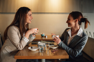 Businesswomen enjoying coffee break, talking and smiling in cafe
