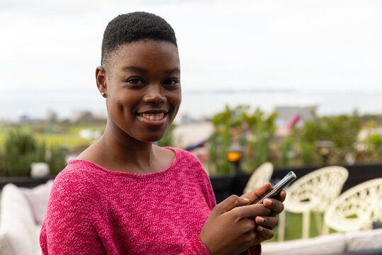 Using smartphone on rooftop, woman in pink sweater attending outdoor gathering