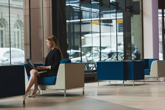 Businesswoman working on laptop in modern office lobby with snowy city view, copy space