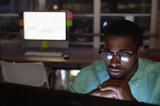 Focused African American man working late on computer in dimly lit office, copy space