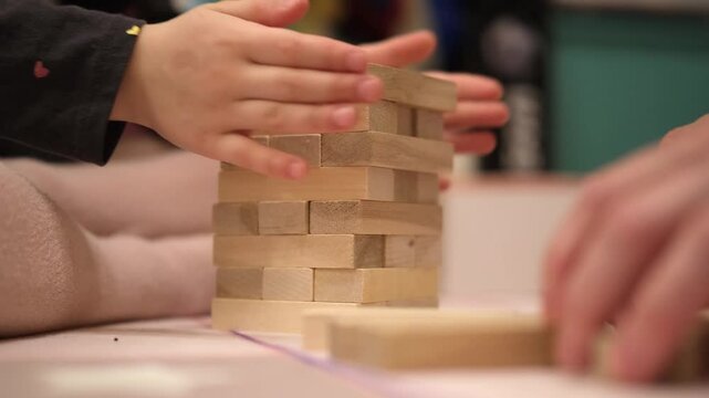 Child's hands carefully stacking wooden blocks into a tower during play. Depicts concentration and fine motor skill development through engaging construction activity.