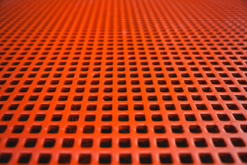 Close-up view of a red metal grid with evenly spaced square holes, creating a geometric and industrial pattern