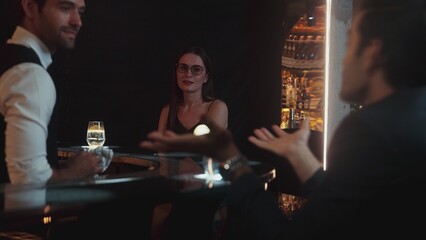 Focusing on beautiful woman guest sitting in special drink gin fizz at luxurious counter bar at vibrant nightlife party atmosphere. Smart bartender wiping glass while talking with customer. Vinosity.