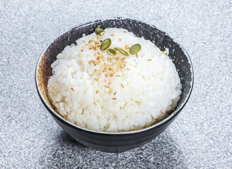 Fragrant rice or Steamed White Rice topped Sesame Seeds, and Pumpkin Seeds, served in black bowl isolated stone background side view of Kong Asian street food