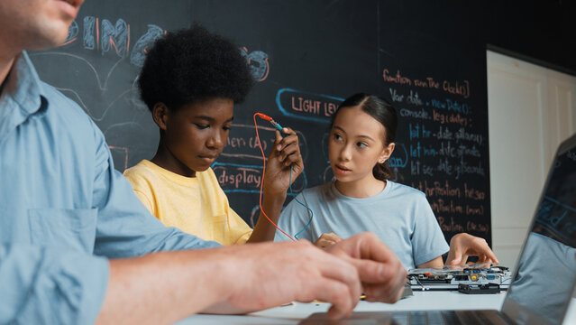 Young student fixing controller while teacher programing engineering code at STEM class. Closeup of instructor hand typing computer while smart girl using electronic tool and blackboard. Edification.