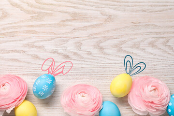 Bright Easter eggs and flowers on wooden table, top view. Some of them with bunny ears