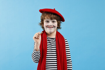 Smiling boy in mime costume with brush on light blue background. Surprise party