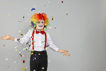 Happy little boy dressed like clown and flying confetti on grey background, space for text....