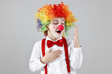Cute little boy in clown wig and red nose on grey background. Surprise party