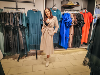 A stylish woman in a beige dress poses confidently in a clothing store, surrounded by elegant...