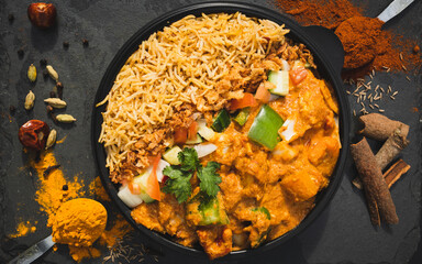 Spiced curry rice meal garnished with fresh vegetables in a black bowl. A deliciously rich and aromatic Indian dish featuring flavorful ingredients, crispy toppings, and a blend of exotic spice