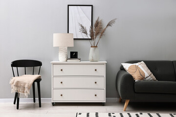 Dresser, chair and couch near light grey wall in room. Interior design