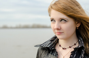 Young woman with red hair and striped shirt gazes thoughtfully. Grey sky and calm water suggest...