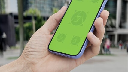 GREEN SCREEN CHROMA KEY Smartphone with green screen held in hand in an urban cityscape with palm trees and buildings, perfect for app or tech displays