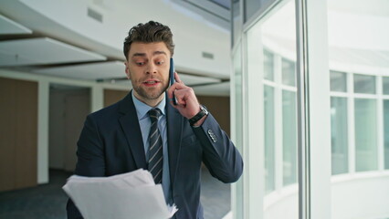 Fototapeta premium Disappointed professional talking smartphone holding documents hallway closeup
