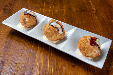 Three crispy, golden Japanese fish balls on a white rectangular plate with three compartments, set on a wooden table. Drizzled with creamy sauce and dark glaze.