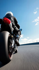 Obraz premium A man is riding a motorcycle on a road. The sky is blue and there are clouds in the background