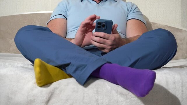 Man sitting on bed with crossed legs wearing mismatched socks using phone