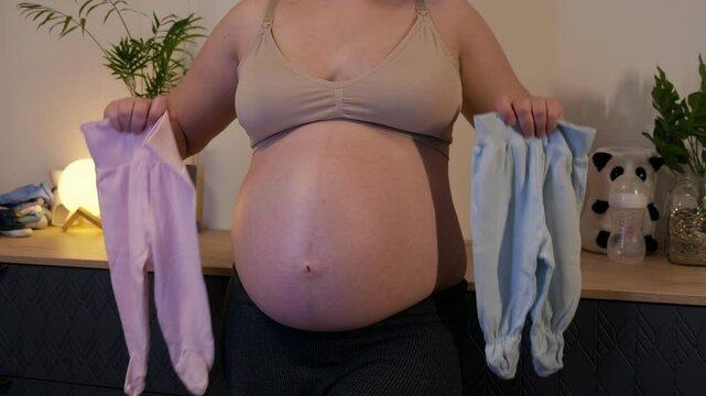 Pregnant woman with big belly in anticipation for the motherhood. Concept of pregnant woman wondering if it a boy or a girl gender with with rompers in hands. Twins