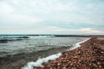 Sandy sea, ocean coast with waves crashing on a sandy shore on a summer day. Vertical natural seaside background. Marine theme. Wavy windy weather.