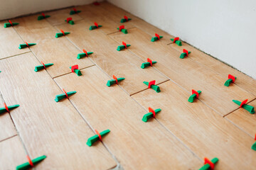 Tile leveling system with plastic clips and wedges. Wood effect narrow tiles installed on floor....