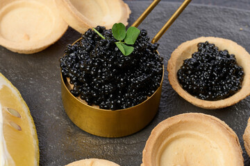 Black sturgeon caviar and empty round tartlets on table, top view