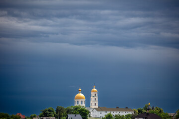 A picturesque town lush greenery, and golden-domed churches in the background. The dramatic sky adds contrast, creating a serene yet moody atmosphere.