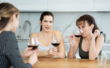 Three women communicate during gatherings, drink wine, joke and laugh. Pleasant meeting of friends,...
