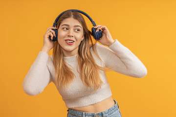 Happy young woman enjoys music with headphones, yellow background visible
