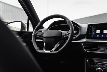 Modern car interior with metal accents. Steering wheel and dashboard of a new vehicle parked near...