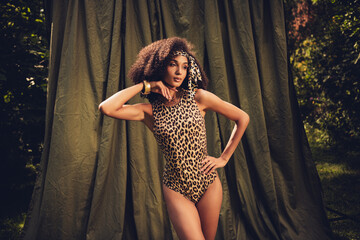 Fashionable woman posing outdoors against a natural backdrop, wearing animal-print attire and...