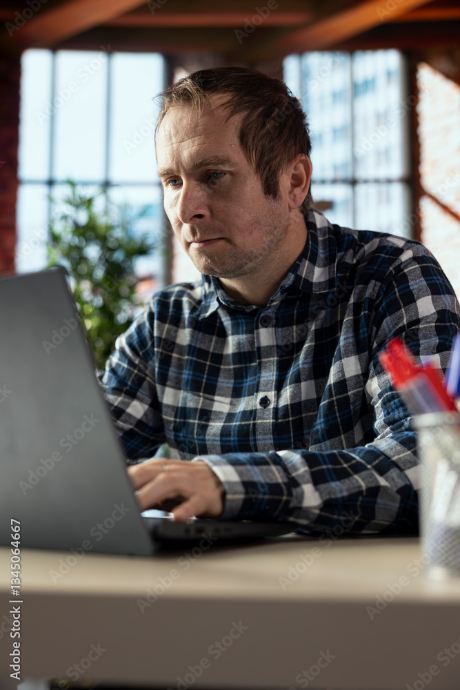 Poster man at home office desk edits documents on laptop, updating reports and files, typing text, formatti