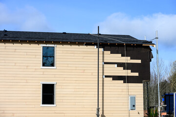New housing construction site, now house with moisture prevention membrane and wood siding being installed with scaffolding, sunny winter day on job site
