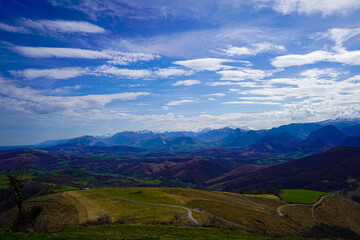 Naklejka premium Winding Roads Along Grassy Hills With Snowy Mountains In The Distance With Cloudy Blue Sky