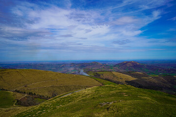 Obraz premium Rolling Grassy Hills With Billowing Smoke and Cloudy Blue Sky