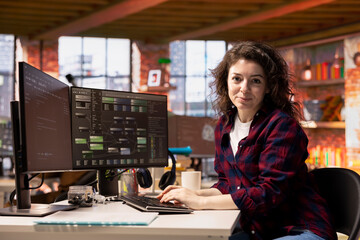 Portrait of smiling woman in startup office designing, coding and debugging applications in...