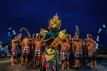 Bali, Indonesia - November 23, 2023: The Kecak dance unfolds as a warrior Ram, adorned in gold, leads a hypnotic chant of bare-chested performers in checkered sarongs, echoing an ancient Hindu epic