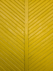 Yellow wooden wall with a symmetrical chevron pattern. The aged texture and worn paint give the facade a rustic and vintage appearance.