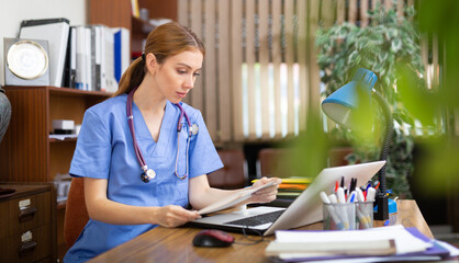 Focused young female doctor working with laptop in clinic office. Modern medicine and healthcare concept..