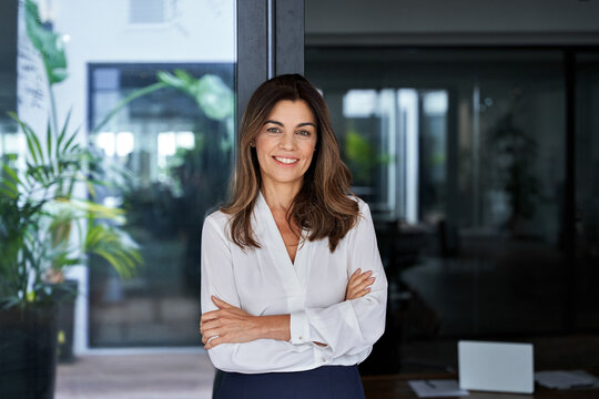 Happy elegant older mature lady posing for portrait standing in office. Beautiful middle aged business woman looking at camera, smiling 45 years old businesswoman leader executive at work.