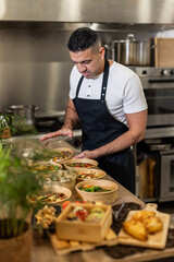 A chef in a black apron packs fresh, healthy takeout meals in eco-friendly bowls. A behind-the-scenes look at a professional kitchen focused on sustainable food service. Vertical copy-space
