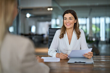Happy mature professional business woman executive hr manager having job interview or business discussion with female applicant or colleague sitting at workplace in corporate office meeting.
