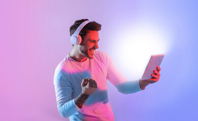 A young man with headphones enthusiastically engages with a tablet, expressing joy and excitement...