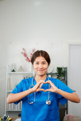 Cheerful healthcare worker in blue scrubs forming a heart shape with hands, symbolizing care and...