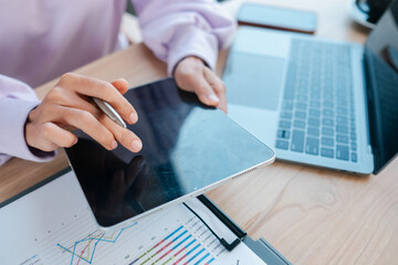 Close-up of a person using a tablet and laptop to analyze business data with charts and graphs in a...