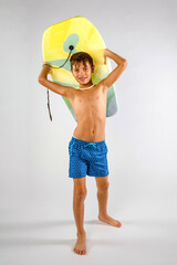 Beach boy wearing swim trunks and a shell necklace, walking to the beach carrying his boogie board...