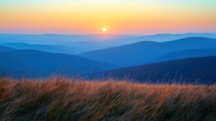 Fototapeta premium Sunset over blue mountains with grass in the foreground, serene view