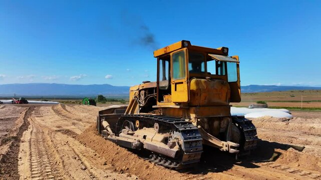 Tracking shot of yellow road grader smoothing gravel surface for highway road. Scraper leveling ground, working at construction. Earthmoving, excavations, digging on soils.