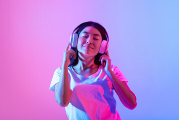 Asian woman is immersed in music while wearing headphones, with a serene expression on her face....